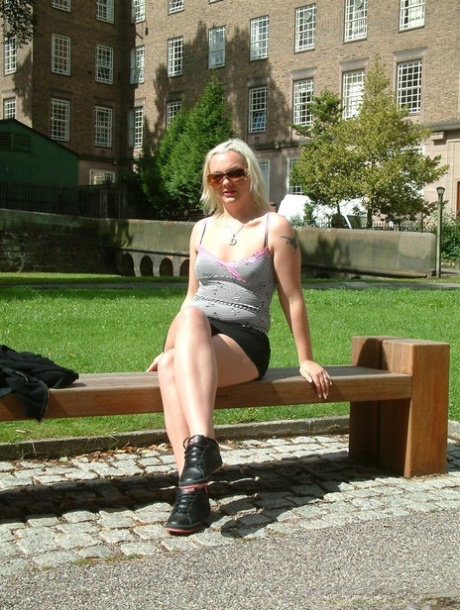 Une blonde expose ses seins et sa chatte sur un banc dans un parc public.