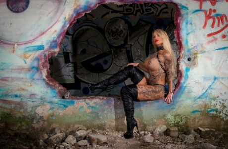 Loira tatuada com modelos de mamas grandes, sozinha em meio a paredes cheias de grafite