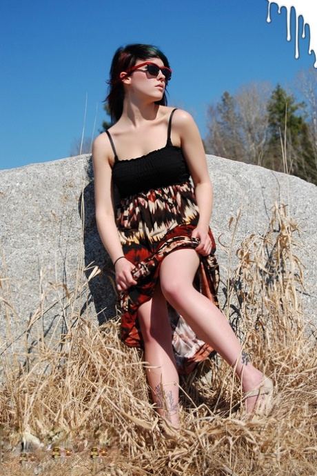 Teen-Amateurin Sabrina Squirts schlüpft oben auf einem Felsbrocken in einem Feld aus ihrem Kleid