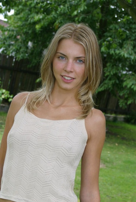 Une jeune blonde aux petits seins met son cul serré et sa fente en valeur sur la pelouse.