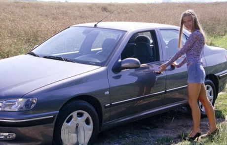 En sexy blondine trer ut bak rattet for å kle seg naken på panseret på bilen.