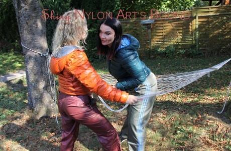 Blond pige binder sin lesbiske elskerinde i vintertøj på en hængekøje i en have
