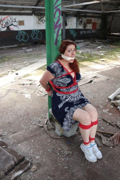 Redhead BBW finds herself gagged & tied to a post while clothed in a warehouse