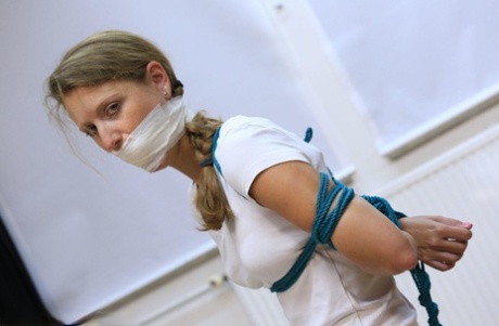 Caucasian female is silenced with a gag while tied to a chair in bare feet