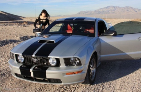 La amateur morena Susy Rocks modela junto a un muscle car durante una actuación segura para el trabajo