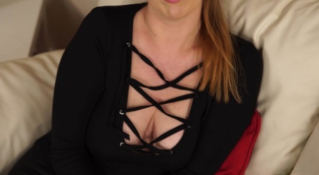 Naturlig rødhåret kvinne viser utringningen sin iført svarte klær i en sofa