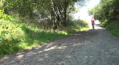 La rubia Delphine se pone en cuclillas para orinar en un camino de grava en el campo