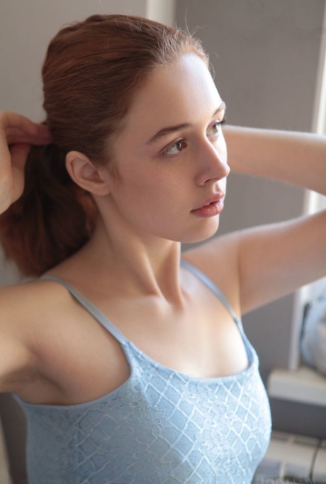 Young redhead Riccarda works free of a dress to pose naked in the kitchen