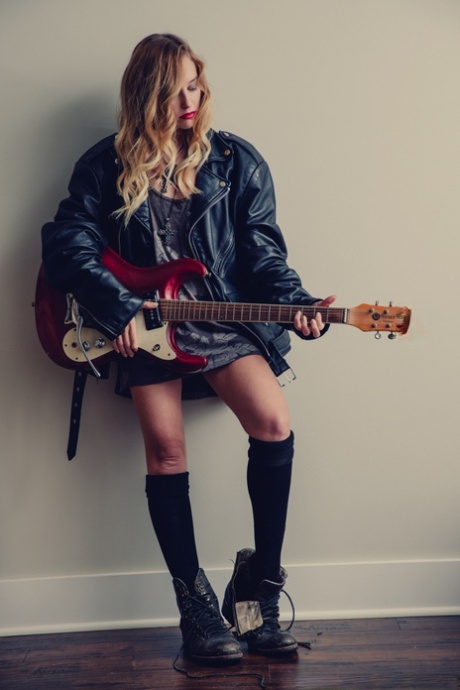 Hete meid Samantha Sterling houdt een gitaar vast terwijl ze naakt in zwarte sokken loopt