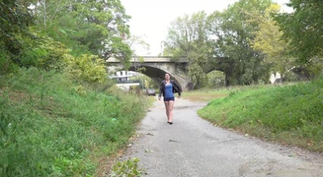 La chica de piernas largas Amanda Hill se baja los pantalones cortos y las bragas para orinar en un camino pavimentado