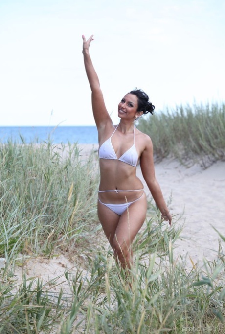 La adolescente de piernas largas Lusee cubre su cuerpo desnudo en la arena de la playa tras perder su bikini
