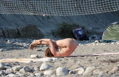 Rapariga flexível faz ioga nua enquanto acampa numa praia