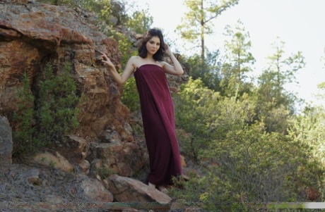 Malena, une adolescente aux pieds nus, enlève une longue robe pour poser nue sur une rive rocheuse.