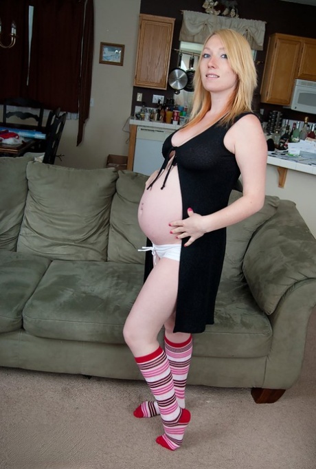 Gravid jente med blondt hår kler seg naken iført knestrømper
