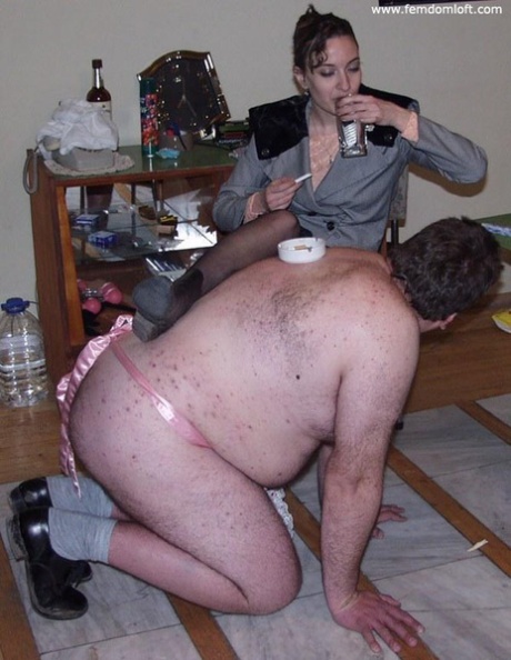 Una mujer dominante tortura a un hombre desnudo con sobrepeso mientras fuma