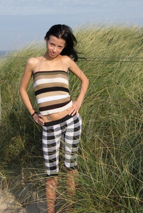 Štíhlá brunetka si drží holý zadek naboso na písečné pláži