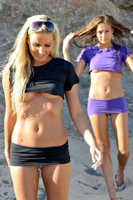 To piger blotter deres bryster og barberede fisser på en sandstrand