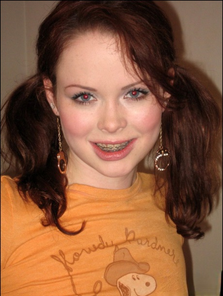 Młoda dziewczyna nosi rude włosy w warkoczach, rozbierając się na łóżku