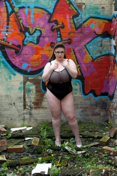 Brunettefettet Gina G viser puppene sine mens hun kler seg naken i nærheten av graffiti.
