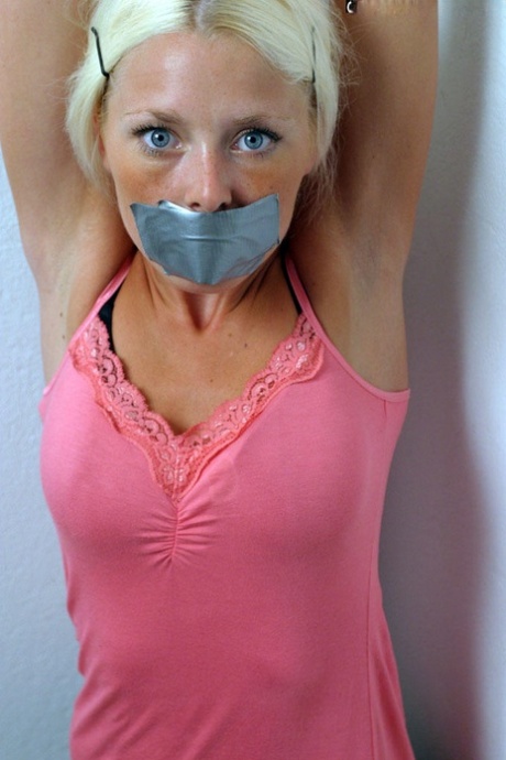 Une blonde habillée est enfermée avec un conduit sur la bouche et les poignets attachés ensemble.