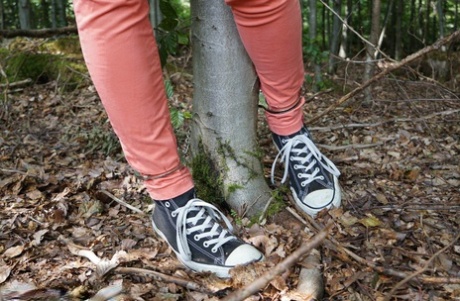 Rapariga vestida com ténis de lona encontra-se algemada a uma árvore num bosque