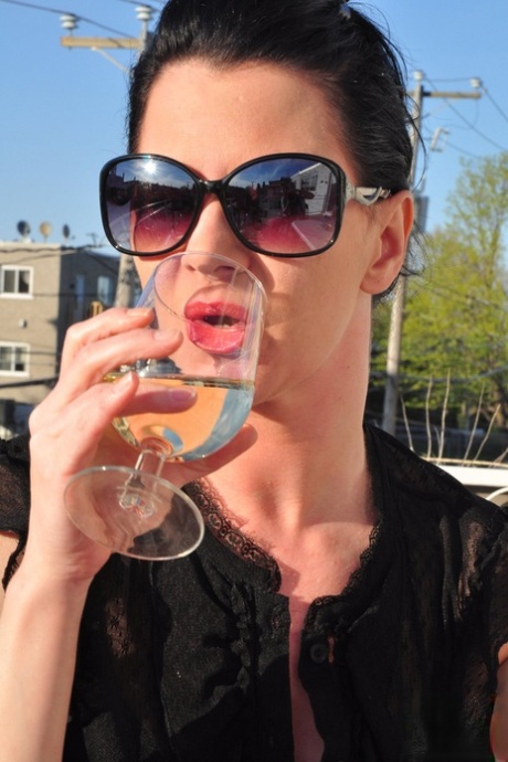 Fully clothed brunette woman smokes and drinks on patio in sunglasses