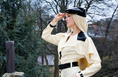 Het blondin visar latexstrumpeband när hon står modell utomhus i gummikläder