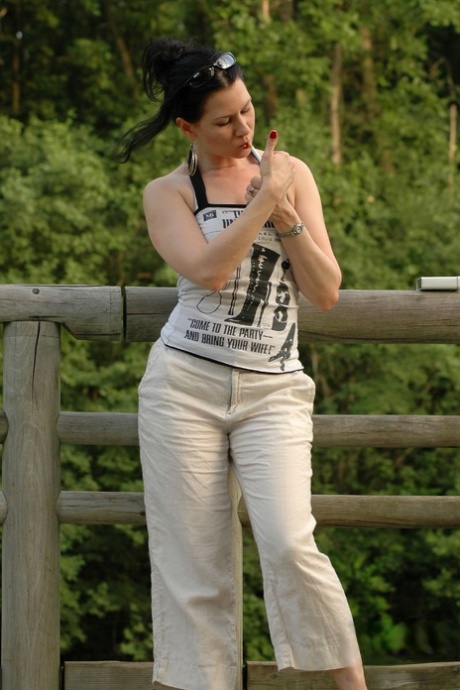 Solo girl smokes a cigarette up against a rail fence while fully clothed