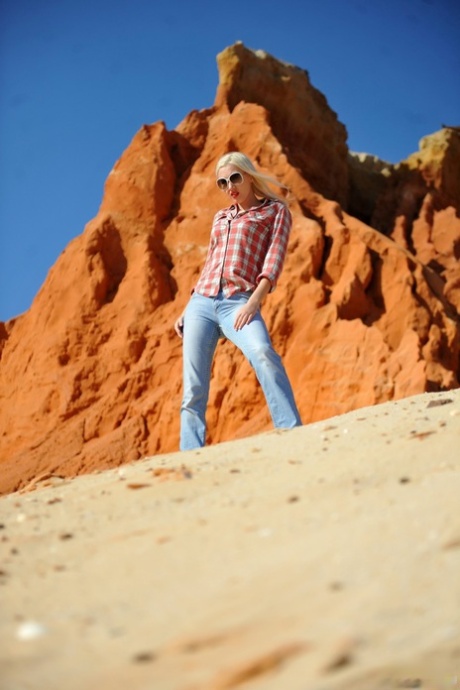 Le mannequin blond Lada Love arbore des lèvres rouges en se dénudant sur des rochers rouges.