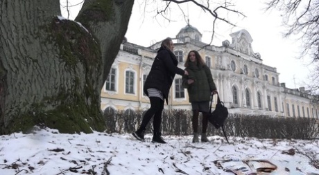 A rapariga loira Masha faz chichi no chão coberto de neve contra uma velha árvore