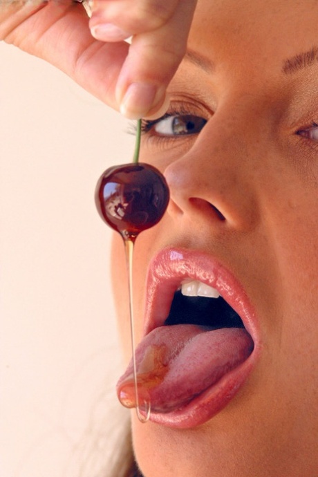 Pretty girl Sandra Shine curls her tongue while sucking juice from a cherry