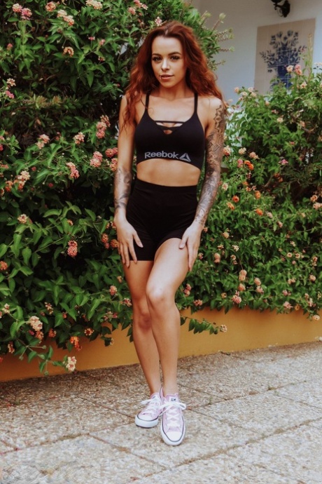 La rousse tatouée Mia Stryker enlève sa tenue de sport devant des buissons en fleurs