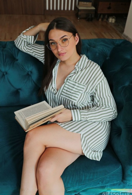 Młoda brunetka Vavilia Cristoff czyta książkę na kanapie, zanim się rozbierze