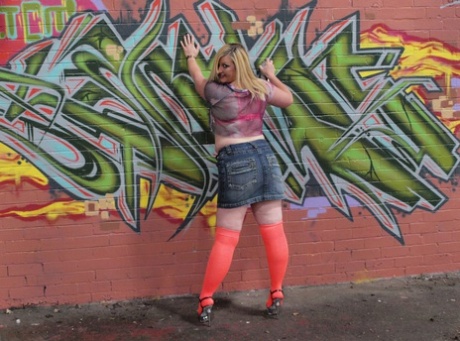 Samantha amadora de pelúcia ajoelha-se em nylons altos em frente ao graffiti
