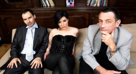 Anastacia Black faz sexo com um casal de homens num sofá.