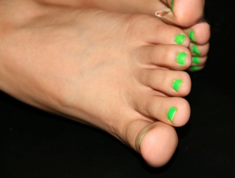 Mujer caucásica luce las uñas de los pies pintadas mientras se frota los pies descalzos