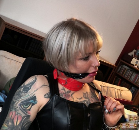 Blond girl Roxxxi Manson struggles against a gag while chained in leather wear