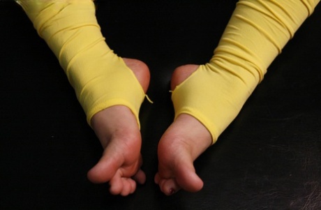 Blank vrouwtje speelt met haar voeten terwijl ze gele beenwarmers draagt