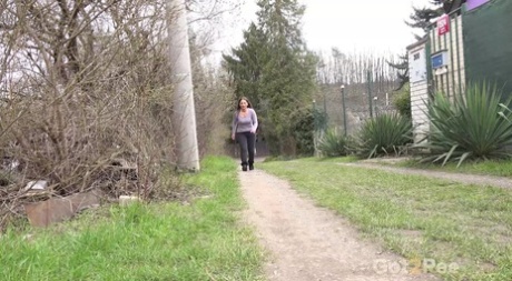 Nicolette Noir pisse en marchant sur un chemin de terre derrière des maisons.