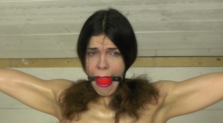 Restrained white girl works up a sweat while struggling against a ball gag