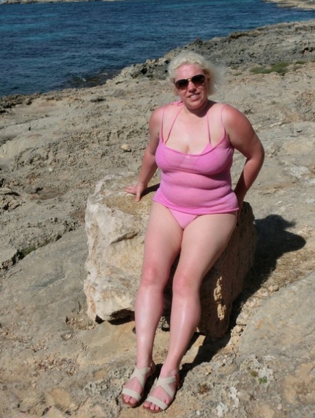 Mollige oudere blonde Barby gaat naakt in zonnebril bij de oceaan
