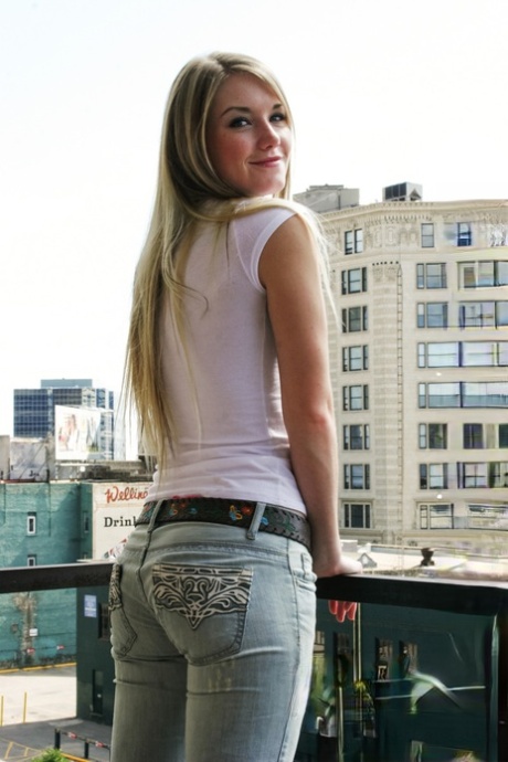 Une amatrice blonde se déshabille sur un balcon en ville en portant des chaussures