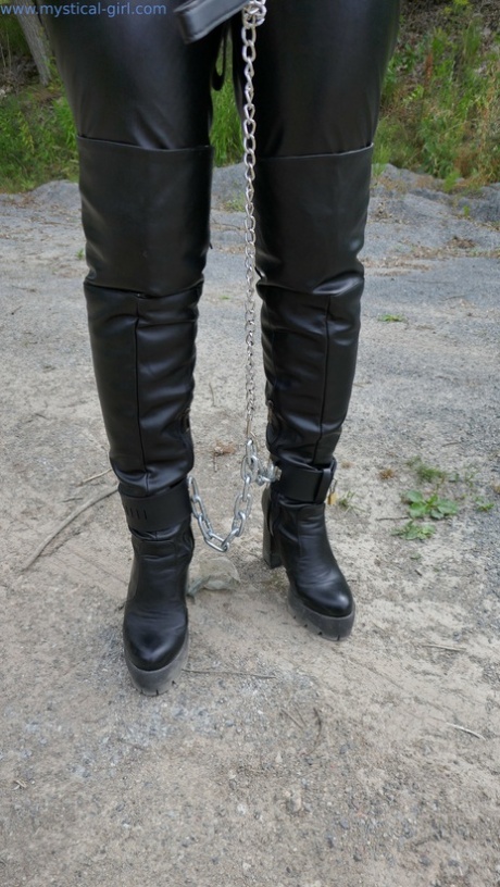 Collared female is restrained with cuffs and chains while wearing leather