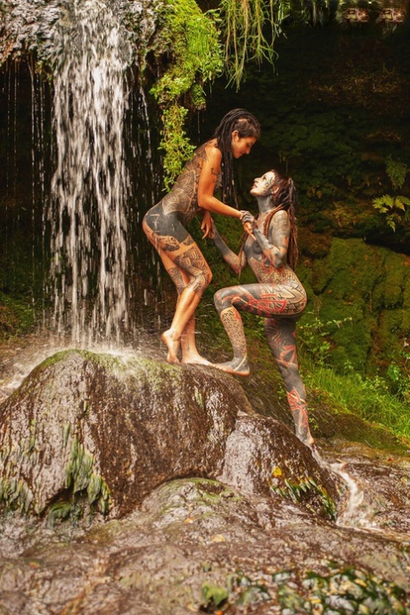 Tungt tatoverte lesber holder rundt hverandre mens de står splitter nakne på en bro.