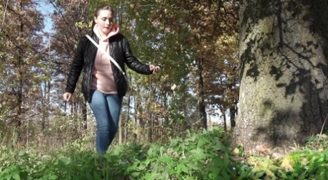 Una ragazza bassina si abbassa i jeans per pisciare accanto a un albero