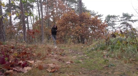 Ragazza vestita si abbassa i pantaloni per pisciare su un sentiero nel bosco