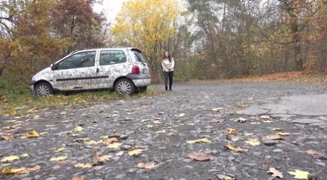 Wit meisje Nicolette Noir pist naast een geparkeerde auto in een bosrijke omgeving