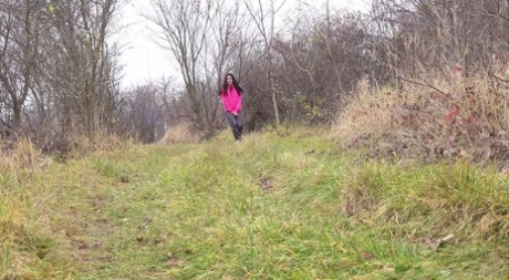 Menina de cabelo escuro puxa as perneiras para baixo para mijar num caminho no bosque