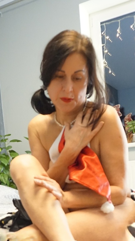 Ältere Brünette Diana Ananta zeigt ihre haarlose Vagina, während sie nackt auf einem Bett liegt