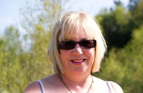 Blonde oma gaat naakt in zonnebril en kousen in een achtertuin
